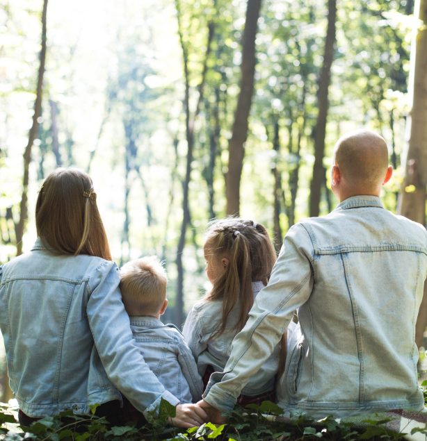 man and woman holding hands together with boy and girl looking at green trees during day